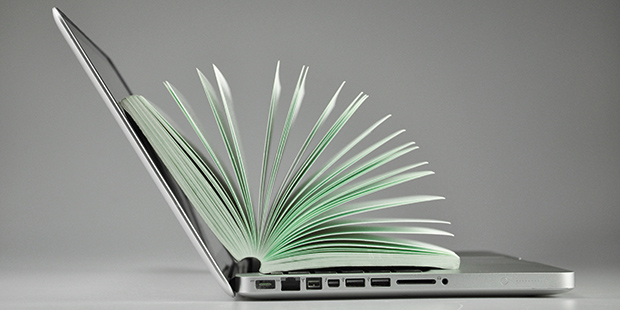 In einem aufgeklappten Laptop ist ein Buch ebenfalls aufgeklappt, sodass die Seiten aufgefächert sind.