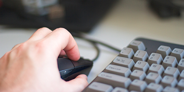 Eine Hand auf einer Computermaus, daneben eine Tastatur