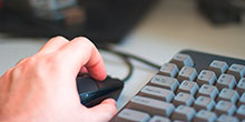 eine Hand auf einer Computer-Maus, dahinter eine Tastatur
