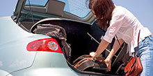 eine Frau verstaut einen Koffer im Kofferraum ihres Autos