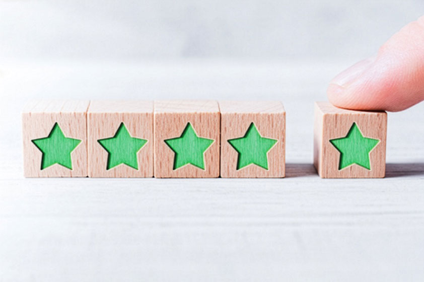 Fünf kleine Holzwürfel mit grünen Sternen. Der fünfte Würfel ist etwas abgerückt und wird von einem Finger gehalten.